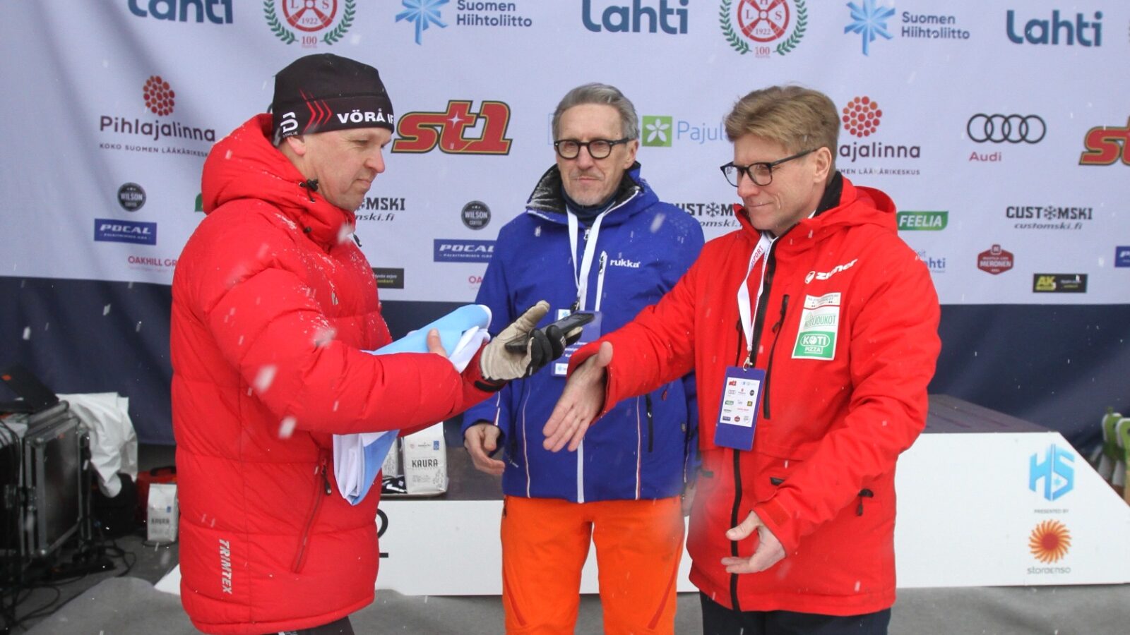 Tor-Leif Häggman, klädd i röd jacka och svart Vörå IF mössa tar emot flaggan av arrangörerna 2023